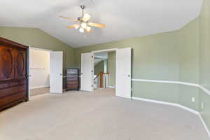 Unfurnished bedroom with light carpet, ceiling fan, a spacious closet, and vaulted ceiling