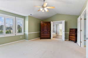 Unfurnished bedroom with ceiling fan, ensuite bathroom, light carpet, and vaulted ceiling