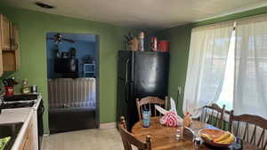 Kitchen with white gas stove, black refrigerator, a textured ceiling, and light brown cabinetry