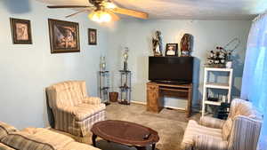 Carpeted living room with ceiling fan and a textured ceiling