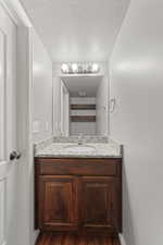 Main floor half bathroom with hardwood / wood-style floors, vanity, and a textured ceiling