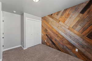 Unfurnished bedroom featuring dark carpet, wooden walls, and a closet