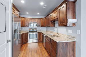 Kitchen with INCLUDED stainless steel appliances, light stone counters, light hardwood / wood-style floors, and sink