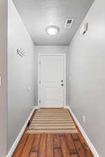 Doorway featuring a textured ceiling and dark wood-type flooring