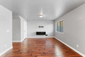 Unfurnished living room featuring dark wood-type flooring and heating unit