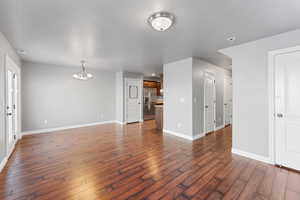 Unfurnished living room featuring a textured ceiling, dark hardwood / wood-style flooring, and an inviting chandelier