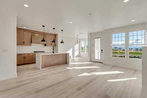 Kitchen with gas cooktop cabinet vent hood, decorative light fixtures, and light flooring