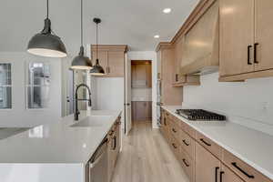 Kitchen with gas cooktop cabinet vent hood, decorative light fixtures, and light flooring