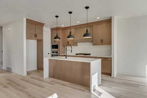 Kitchen with gas cooktop cabinet vent hood, decorative light fixtures, and light flooring