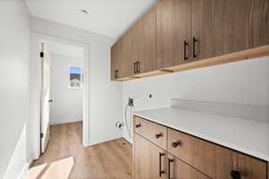 Washroom featuring hookup for an electric dryer, light hardwood / wood-style floors, cabinets, and hookup for a washing machine