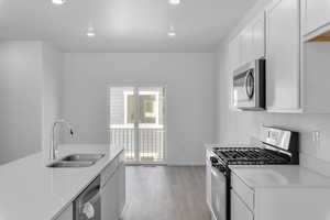 Kitchen with sink, white cabinets, stainless steel appliances, and light wood-type flooring