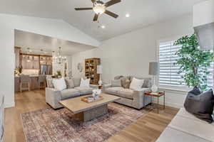 Living room featuring ceiling fan with notable chandelier, lofted ceiling, and light wood-type flooring