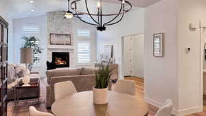 Dining space with ceiling fan with notable chandelier, hardwood / wood-style floors, a textured ceiling, and a stone fireplace