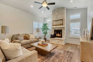 Living room with a stone fireplace, ceiling fan, high vaulted ceiling, and light wood-type flooring