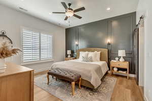 Bedroom featuring light wood-type flooring, a barn door, and ceiling fan