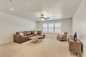 Living room with a textured ceiling, light colored carpet, and ceiling fan