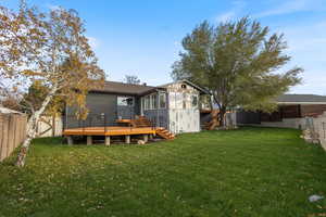 Back of property featuring a lawn, a wooden deck, and a sunroom