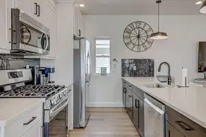 Kitchen with stainless steel appliances, white cabinetry, hanging light fixtures, and sink