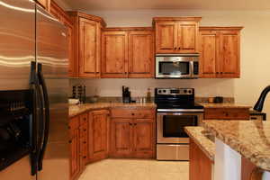 Kitchen featuring light stone countertops, appliances with stainless steel finishes, light tile patterned floors, and ornamental molding