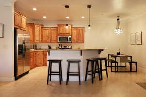 Kitchen featuring hanging light fixtures, light stone countertops, an island with sink, and appliances with stainless steel finishes