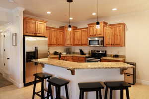 Kitchen with light stone countertops, appliances with stainless steel finishes, a kitchen breakfast bar, and pendant lighting