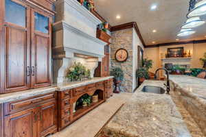 Kitchen with light stone countertops, crown molding, sink, and hanging light fixtures