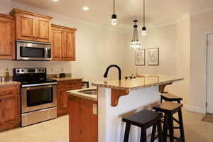 Kitchen with a kitchen island with sink, a breakfast bar, light stone counters, and appliances with stainless steel finishes