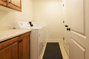 Clothes washing area featuring cabinets, light tile patterned floors, and washer and clothes dryer