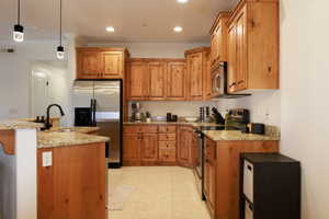 Kitchen with light stone countertops, sink, crown molding, pendant lighting, and appliances with stainless steel finishes