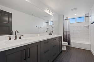 Full bathroom with vanity, toilet, shower / bathtub combination with curtain, and wood-type flooring