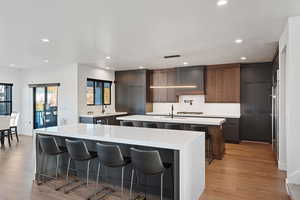 Kitchen featuring sink, hanging light fixtures, light hardwood / wood-style floors, a kitchen bar, and a kitchen island with sink