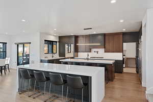 Kitchen featuring sink, hanging light fixtures, light hardwood / wood-style flooring, an island with sink, and a kitchen bar