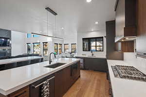 Kitchen featuring sink, hanging light fixtures, beverage cooler, wall chimney range hood, and light wood-type flooring