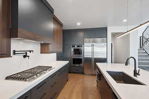 Kitchen with light wood-type flooring, custom range hood, dark brown cabinets, stainless steel appliances, and sink