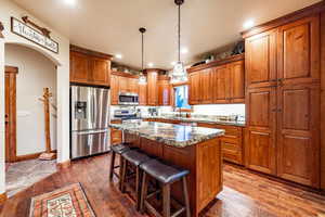 Kitchen with stainless steel appliances, a kitchen island, dark wood-type flooring, and light stone counters