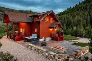 Rear view of property with a lawn, a wooden deck, a patio area, an outdoor fire pit, and a hot tub