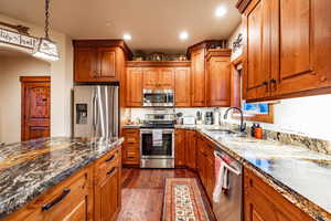 Kitchen with sink, dark wood-type flooring, stainless steel appliances, pendant lighting, and dark stone counters