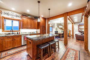 Kitchen featuring a kitchen bar, dark hardwood / wood-style flooring, dark stone counters, dishwasher, and a kitchen island