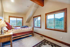 Carpeted bedroom featuring a mountain view, vaulted ceiling with beams, and multiple windows