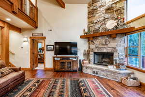 Living room with a stone fireplace, dark hardwood / wood-style flooring, and beam ceiling