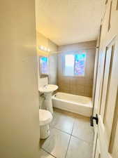 Bathroom with toilet, tile patterned flooring, a textured ceiling, and tiled shower / bath