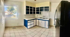 Kitchen with tasteful backsplash, black fridge, ceiling fan, light tile patterned floors, and white cabinetry