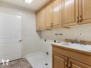 Clothes washing area with cabinets, light tile patterned floors, hookup for an electric dryer, and sink