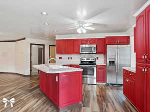 Kitchen with appliances with stainless steel finishes, backsplash, a kitchen island with sink, sink, and wood-type flooring