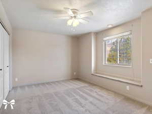 Empty room with ceiling fan, light colored carpet, and a textured ceiling