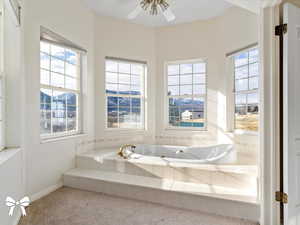 Bathroom with a relaxing tiled tub, ceiling fan, and a healthy amount of sunlight