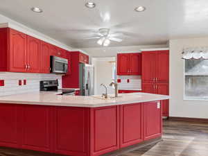 Kitchen with dark wood-type flooring, sink, decorative backsplash, ceiling fan, and appliances with stainless steel finishes