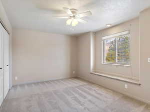 Empty room featuring ceiling fan, light colored carpet, and a textured ceiling