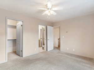 Unfurnished bedroom with light carpet, a walk in closet, ceiling fan, connected bathroom, and a closet