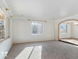 Carpeted spare room featuring ornamental molding and a chandelier